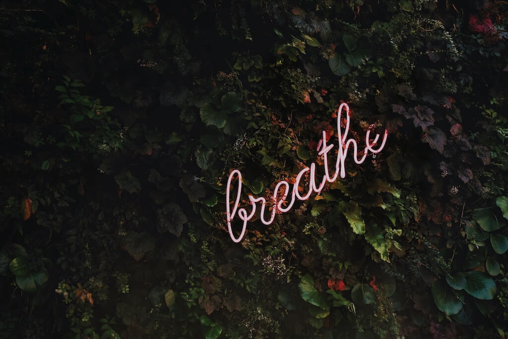 neon sign in lowercase cursive that reads, "breathe"