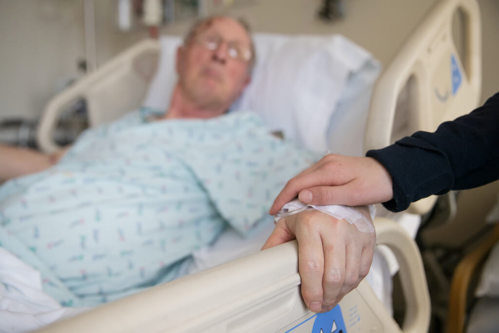 Man in hospital bed, hand on arm
